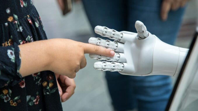 A child touching the finger of a white robotic hand