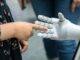 A child touching the finger of a white robotic hand